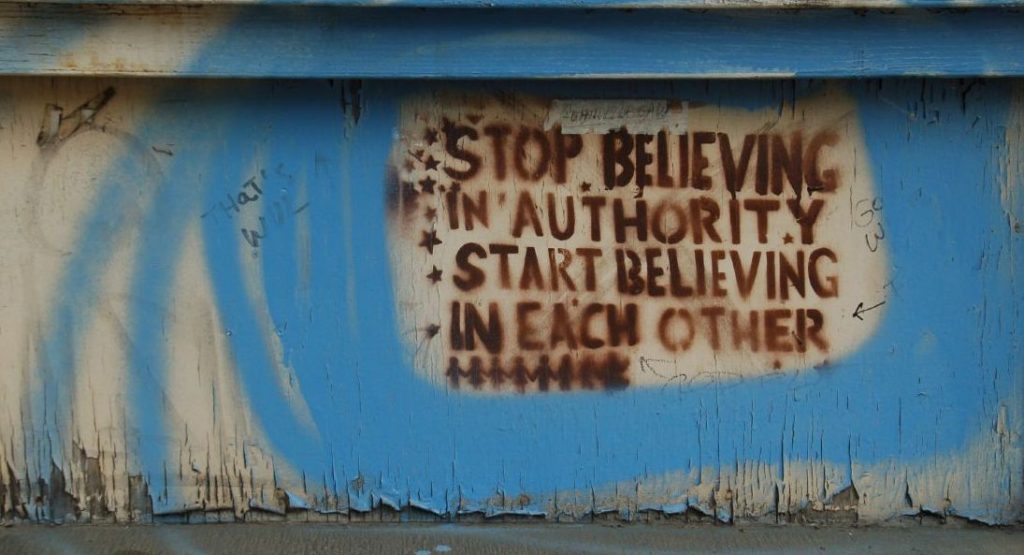 graffiti on a wall saying: "Stop believing in authority, start believing in each other."