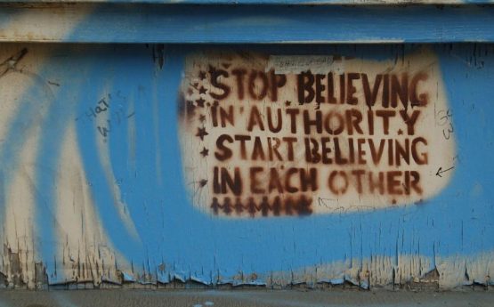 graffiti on a wall saying: "Stop believing in authority, start believing in each other."