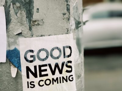Photo of a sign posted to a tree stating "good news is coming"